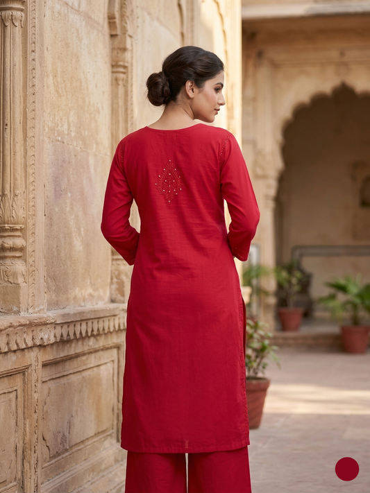 Woman in a red traditional outfit standing in an architectural setting with plants.
