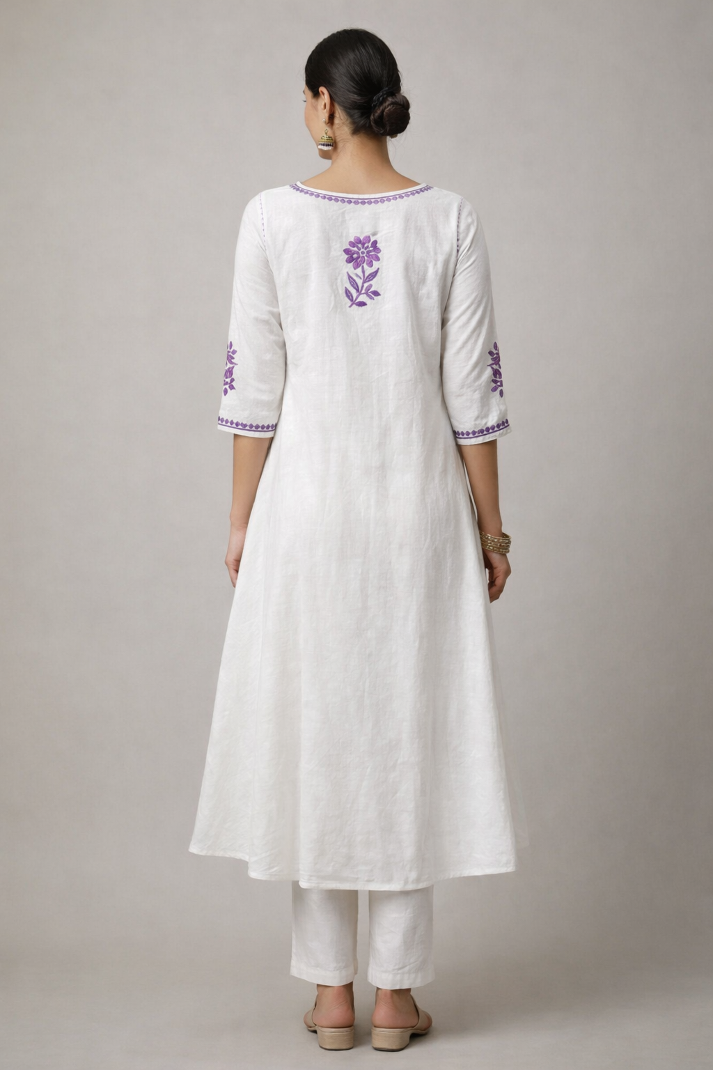 Woman wearing a white kurta with purple floral embroidery on a plain background