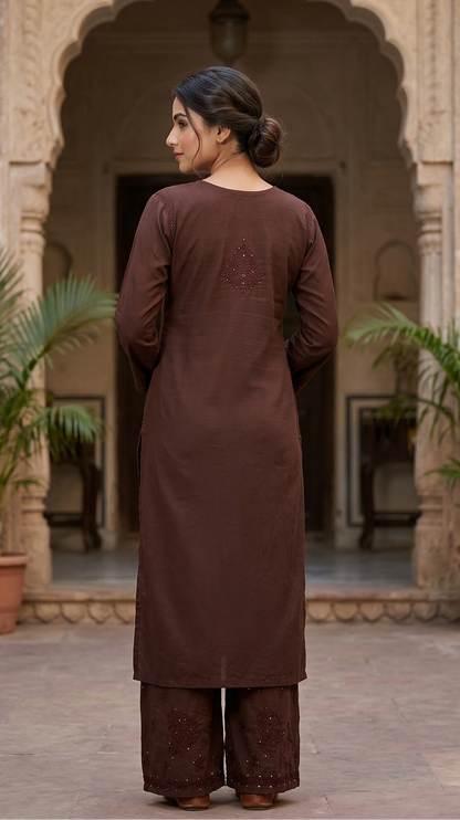 Woman in a brown traditional outfit standing in front of an archway with plants.