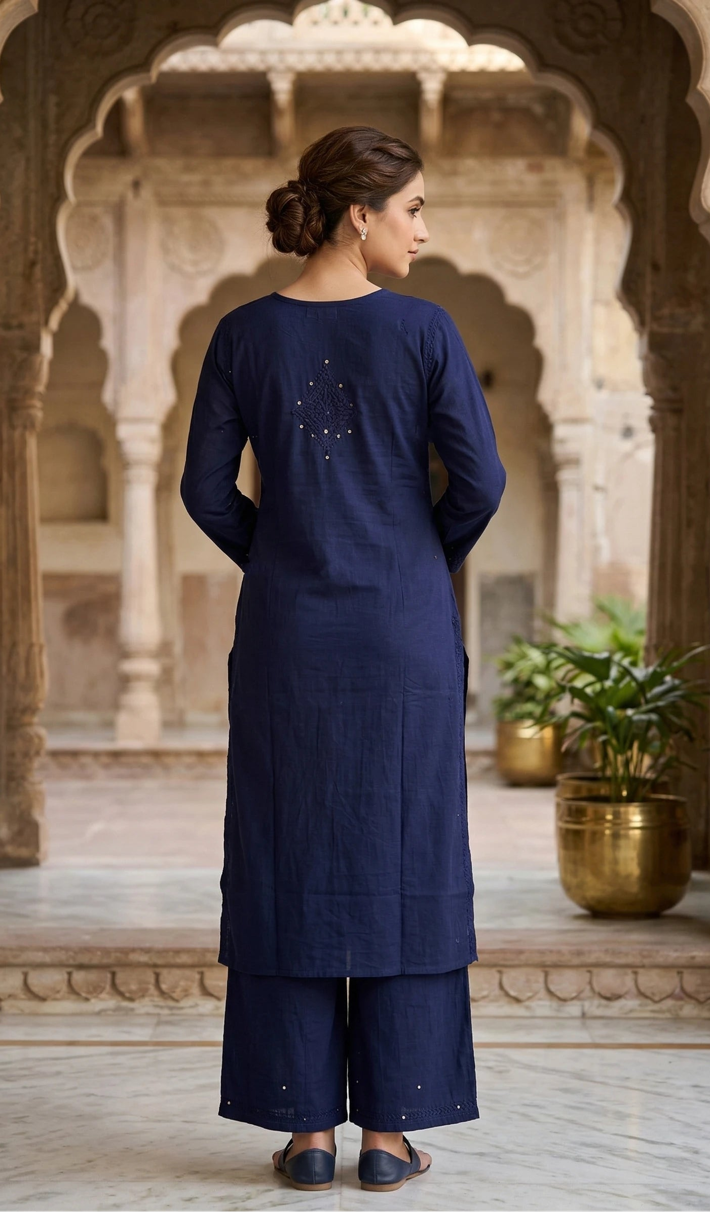 Woman in a navy blue traditional outfit standing in an ornate architectural setting.