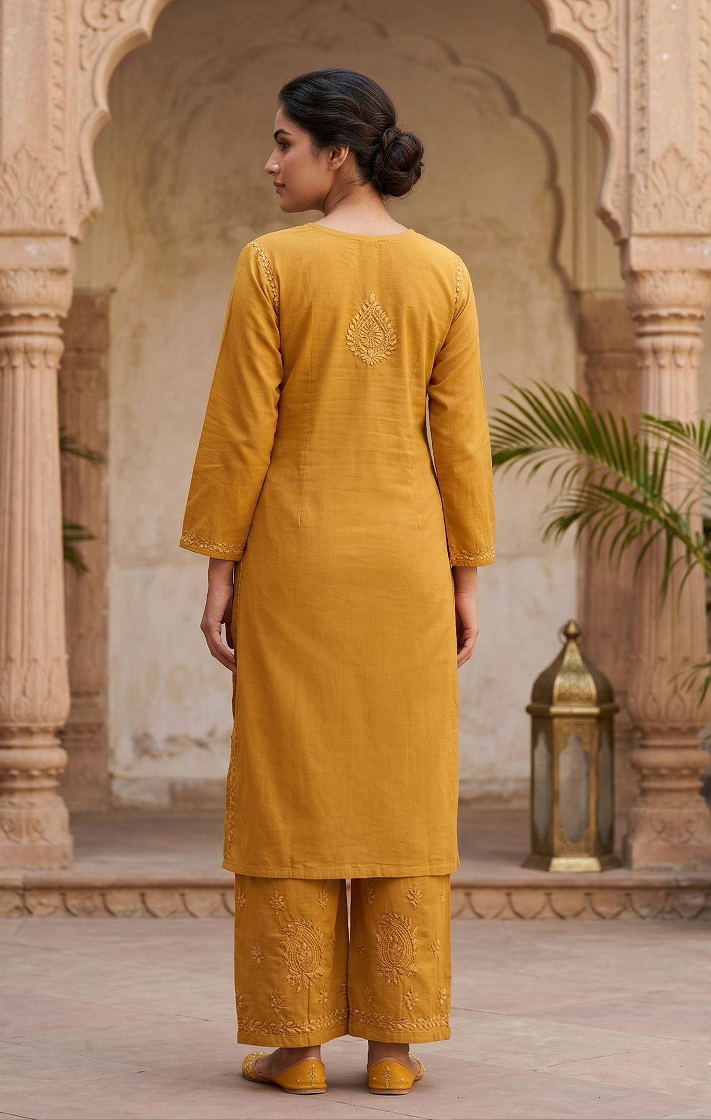 Woman in a mustard yellow traditional outfit standing in an ornate courtyard.