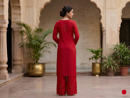 Woman in a red traditional outfit standing in an architectural setting with plants.